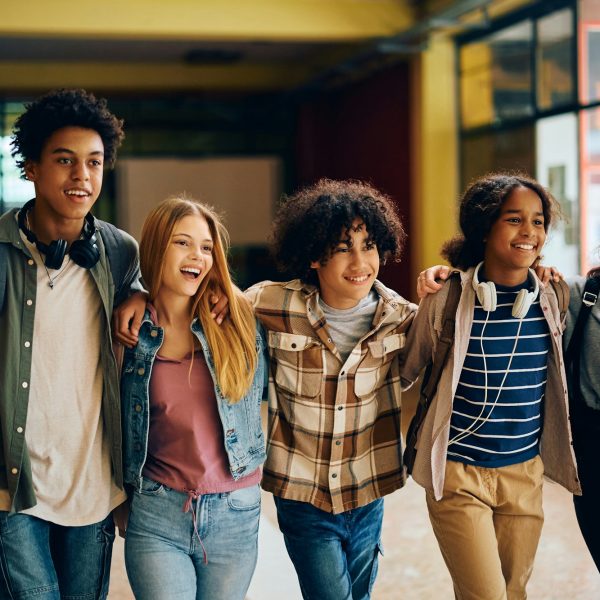 Cheerful high school students walking embraced through the hallway.