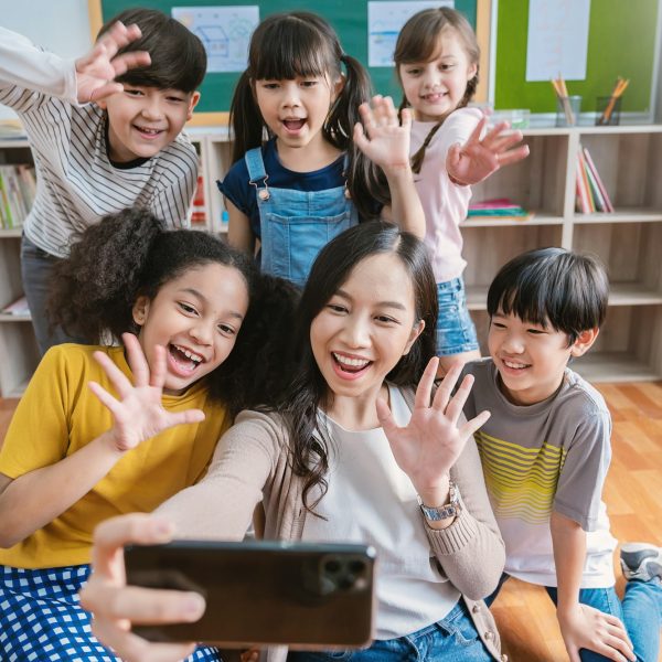 Portrait of teacher and student using smartphone selfie say hi at elementary school
